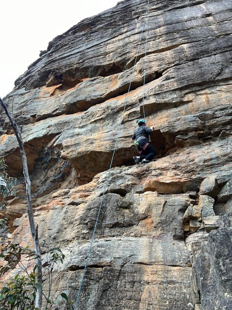 Dr Mara Hickey climbing a tall cliff face on rope